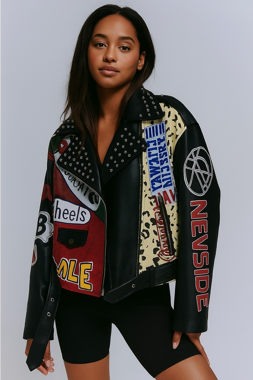 Femme métisse portant une veste biker en simili cuir patchwork avec clous, posant en studio.